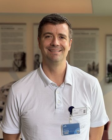 Ein Mann in einem weißen Poloshirt steht in einem modernen Raum mit Pflanzen und Informationswänden im Hintergrund.